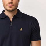 Close-up of the chest and collar of the navy blue polo shirt, featuring the gold embroidered logo and zipper.