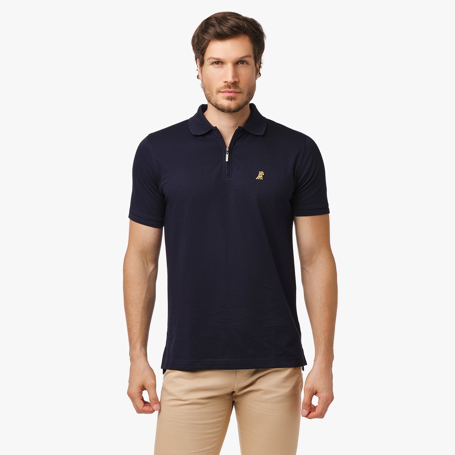 Man wearing a navy blue polo shirt with a gold embroidered logo on the left chest and a zipper detail, paired with beige pants.