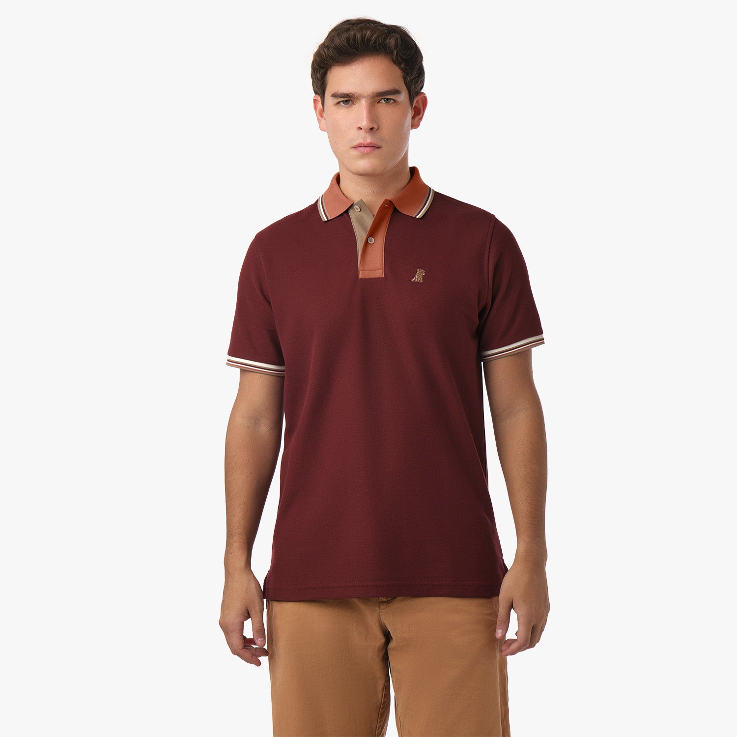  A man standing, wearing a burgundy polo shirt with a brown collar and beige trim, paired with brown shorts.