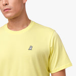 Close-up of the upper chest area of the light yellow t-shirt, focusing on the small embroidered animal logo near the neckline.