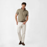 Full-body view of a man wearing the olive polo shirt and white pants: The man is standing in a relaxed pose, showing the overall fit of the shirt paired with white pants.