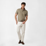 Full-body view of a man wearing the olive polo shirt and white pants: The man is standing in a relaxed pose, showing the overall fit of the shirt paired with white pants.