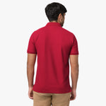 A rear view of a man wearing the red polo shirt and beige pants.