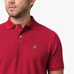 Close-up of a man wearing the red polo shirt, showing the collar and the small golden embroidered logo on the chest.