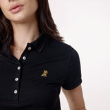 Close-up of the woman’s face and chest, highlighting the collar and gold logo detail on the polo shirt.