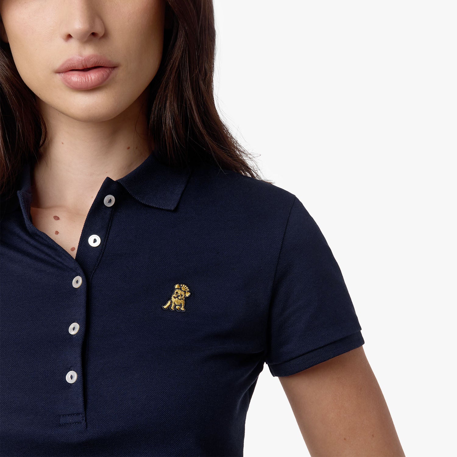 Close-up of the woman’s face and chest, highlighting the collar and gold logo on the navy blue polo shirt.