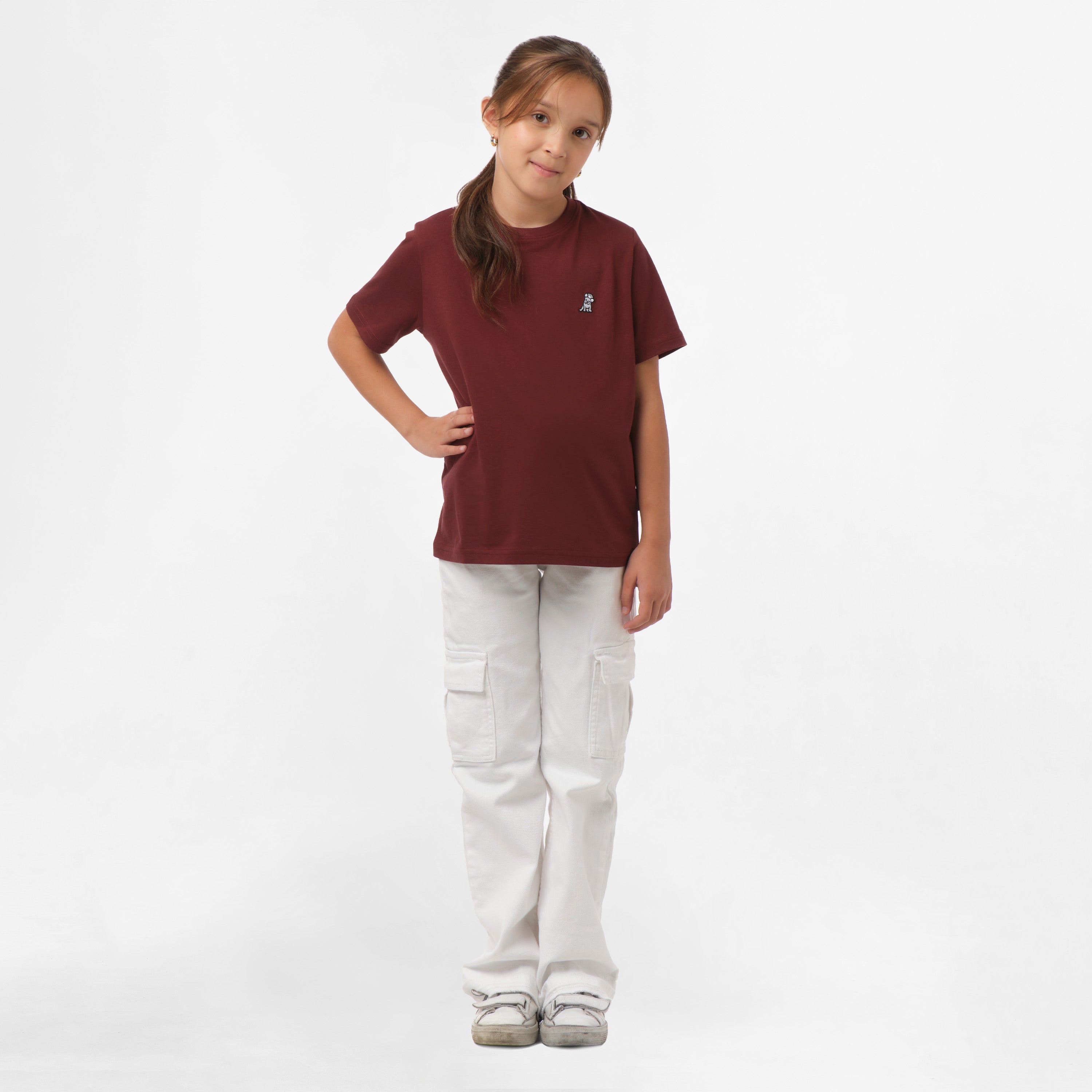 Full-body view of a girl wearing the maroon t-shirt and white pants, standing with one hand on her hip.