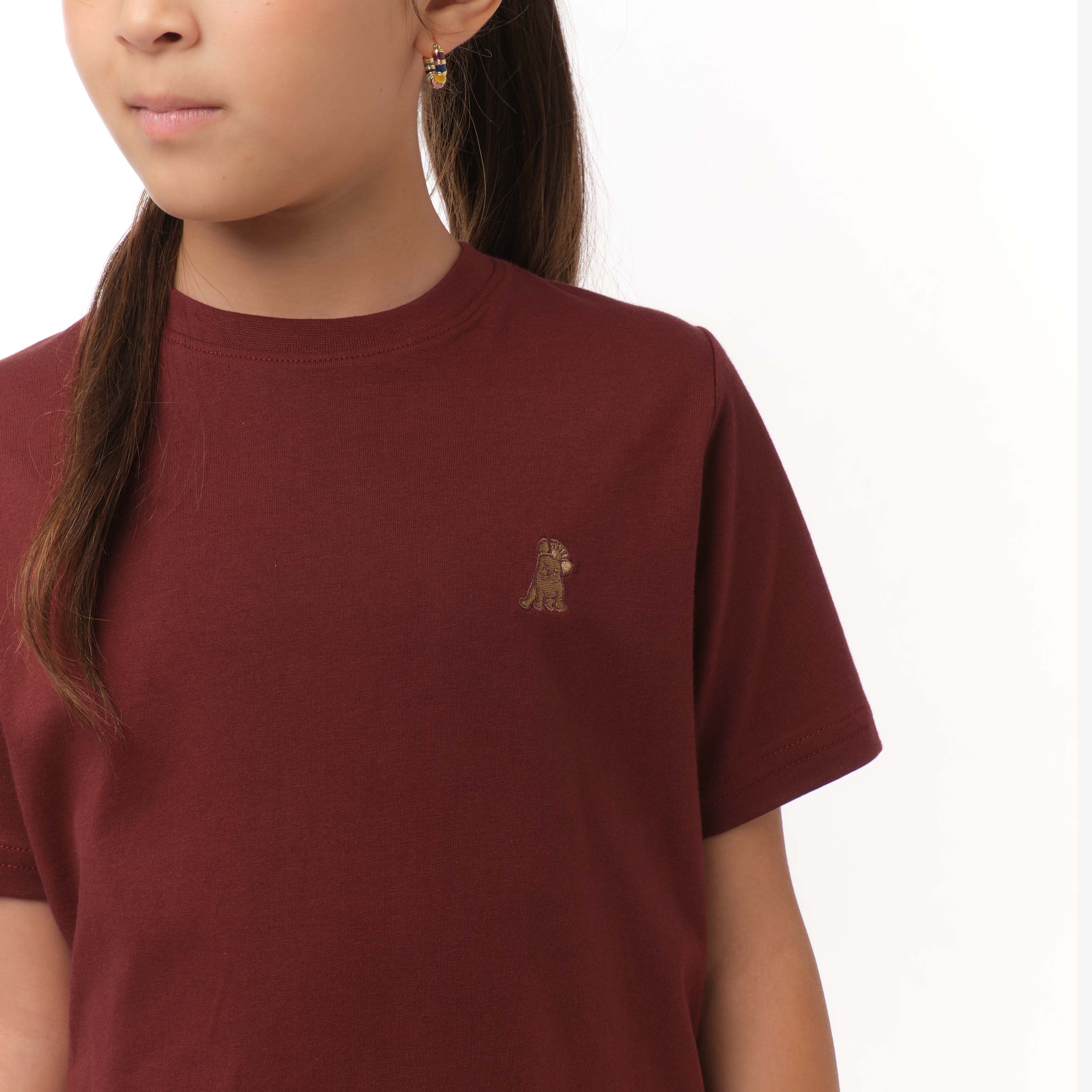 Close-up front view of a girl wearing the maroon t-shirt with a small yellow embroidered logo on the chest.