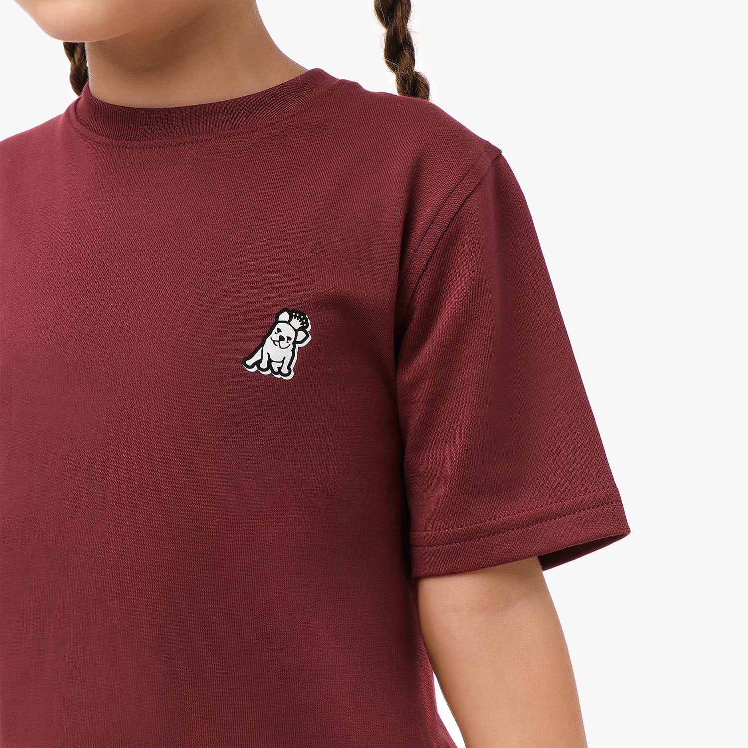  Close-up front view of a girl wearing the maroon t-shirt with a small embroidered logo on the chest.