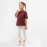 Girl standing while wearing the maroon t-shirt and white pants, facing forward.