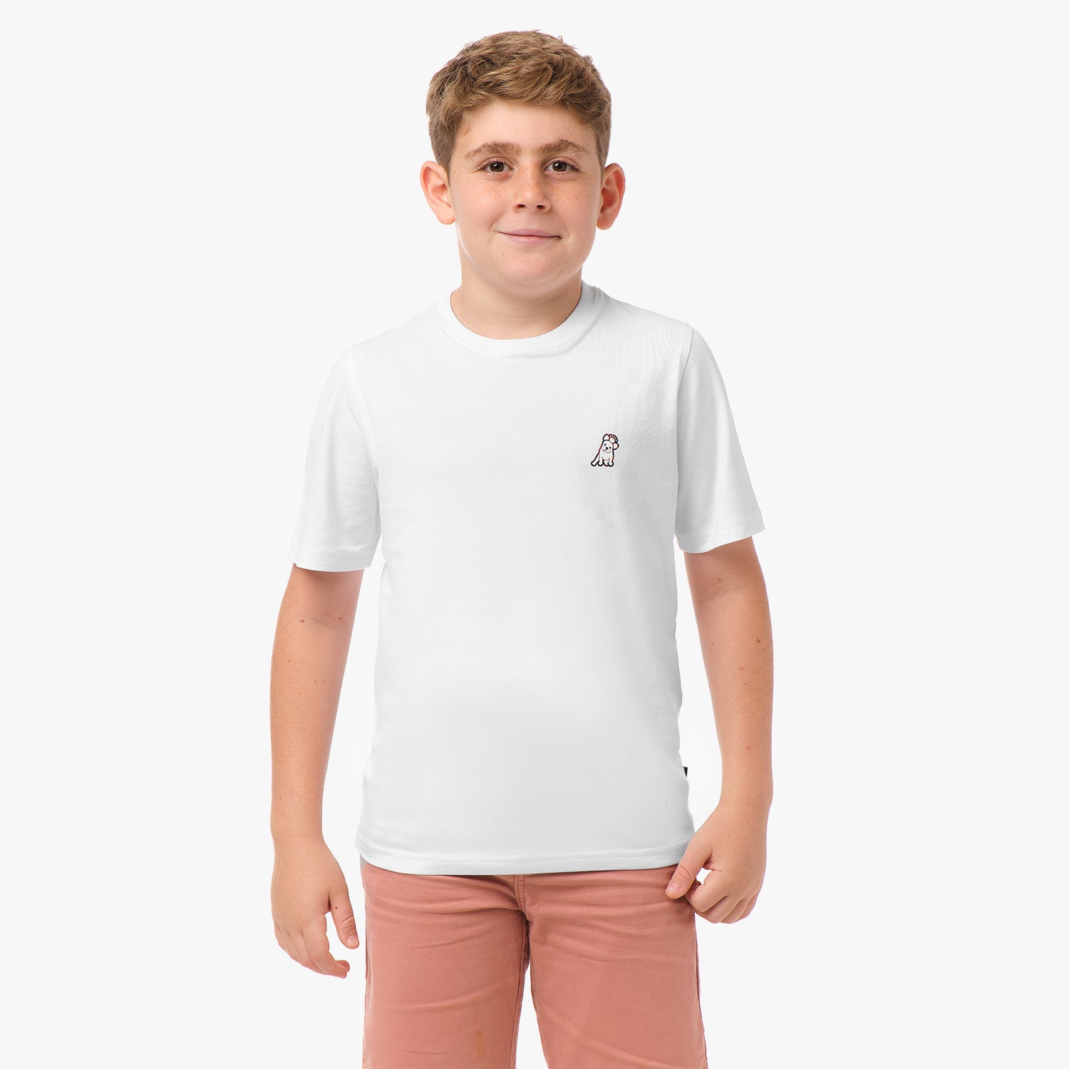 Front view of the boy wearing the white T-shirt with a small embroidered logo on the chest, paired with pink shorts.