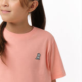 Close-up front view of a girl wearing the light pink t-shirt with a small white embroidered logo on the chest.