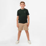 Full-body view of a boy wearing the black t-shirt and beige shorts, standing with his hands in his pockets and legs slightly apart.