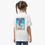 Rear view of a girl with braids wearing a white t-shirt featuring a large colorful graphic of a dog with stacked items and a beach scene.