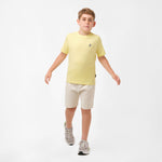 Full-body view of a boy wearing the light yellow t-shirt and light beige shorts, walking forward with both hands slightly raised.