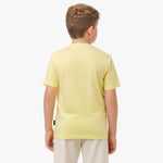 Rear view of a boy wearing the light yellow t-shirt, standing with his hands behind his back.