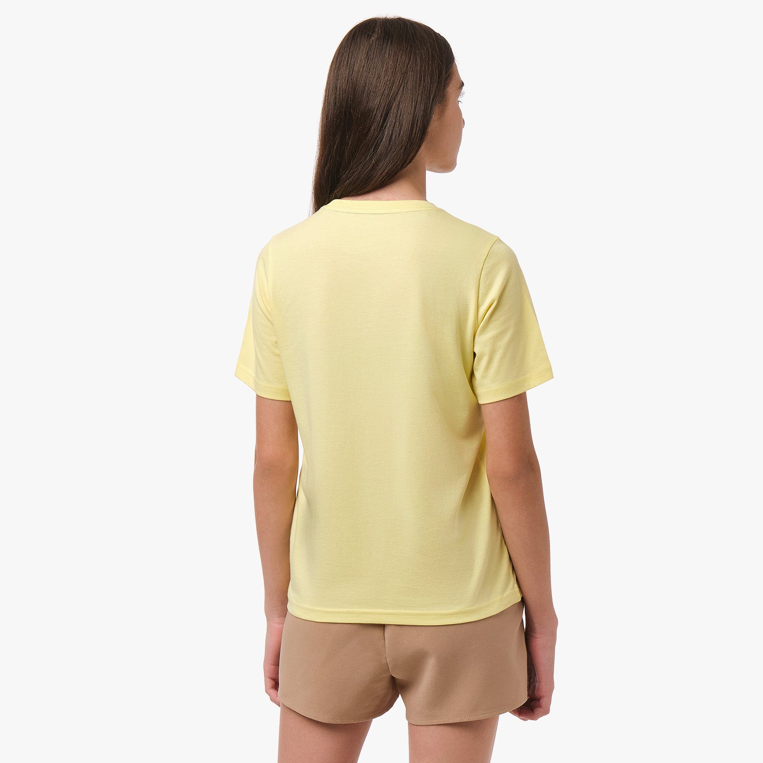 Rear view of a girl wearing the light yellow t-shirt, standing with her hands behind her back.