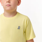 Close-up front view of a boy wearing the light yellow t-shirt with a small white embroidered logo on the chest.