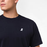 Person wearing a navy blue t-shirt with a small white logo on a plain background