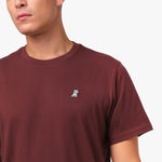 A close-up of the chest area of the maroon t-shirt, highlighting the small embroidered graphic, which appears to be a dog or character.