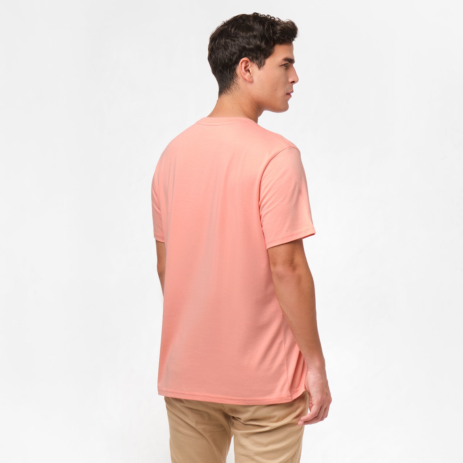 Back view of the man wearing the light pink t-shirt, standing with his arms at his sides, paired with beige pants.