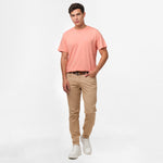 A full-body image of the man wearing the light pink t-shirt and beige pants, standing in a relaxed posture.