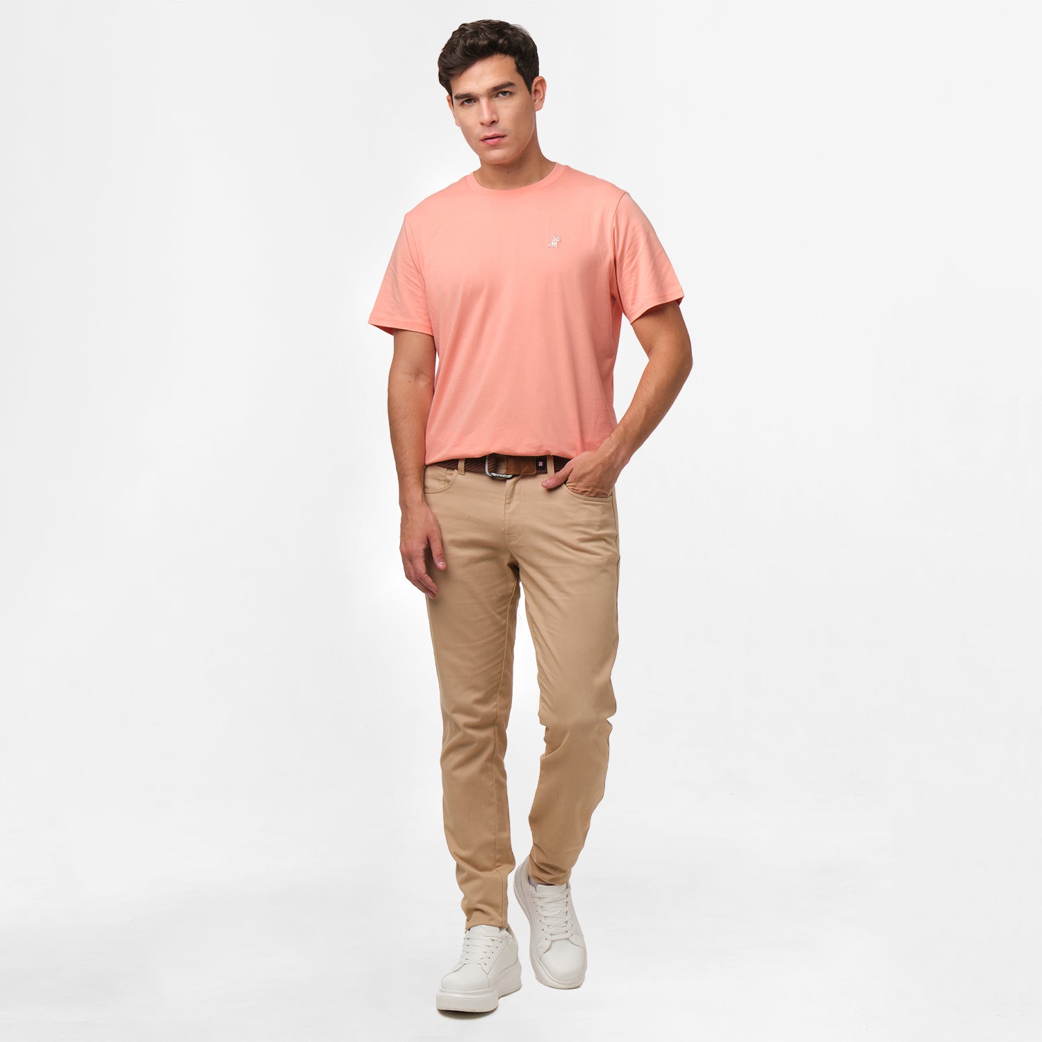 A full-body image of the man wearing the light pink t-shirt and beige pants, standing in a relaxed posture.