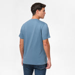 Back view of the man wearing the blue t-shirt, standing with his arms at his sides, paired with dark blue jeans.