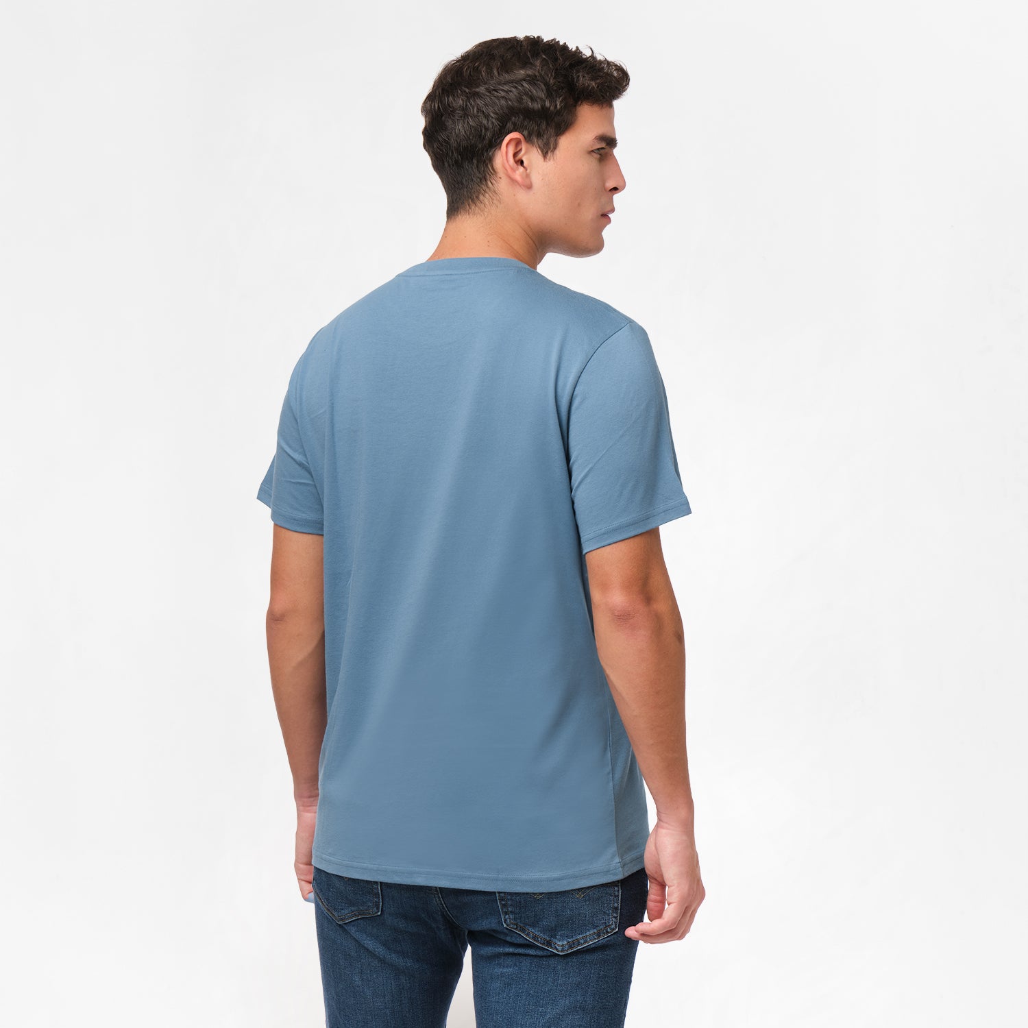 Back view of the man wearing the blue t-shirt, standing with his arms at his sides, paired with dark blue jeans.