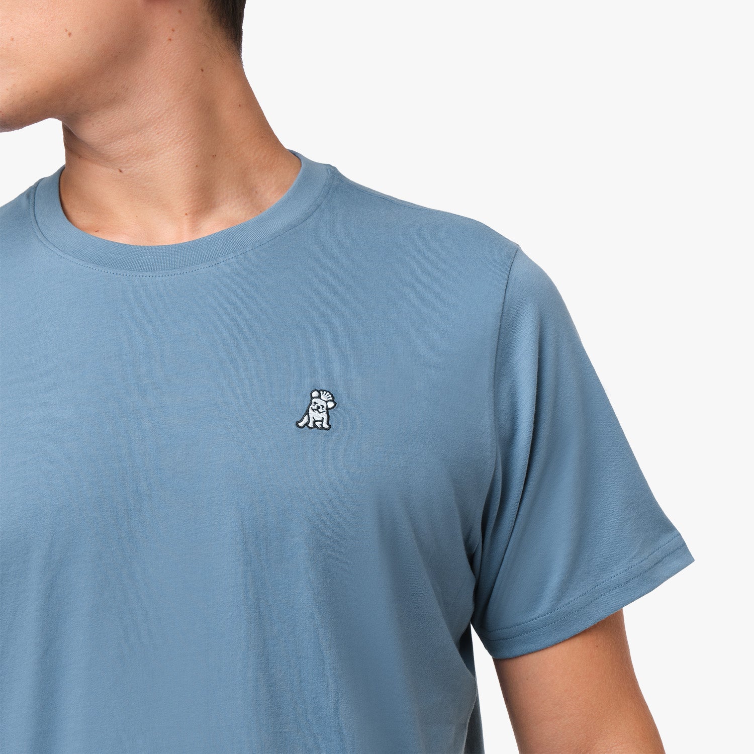 Close-up of the upper chest area of the blue t-shirt, focusing on the small embroidered animal logo near the neckline.