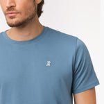 Close-up of the upper chest area of the blue t-shirt, focusing on the small embroidered animal logo near the neckline.