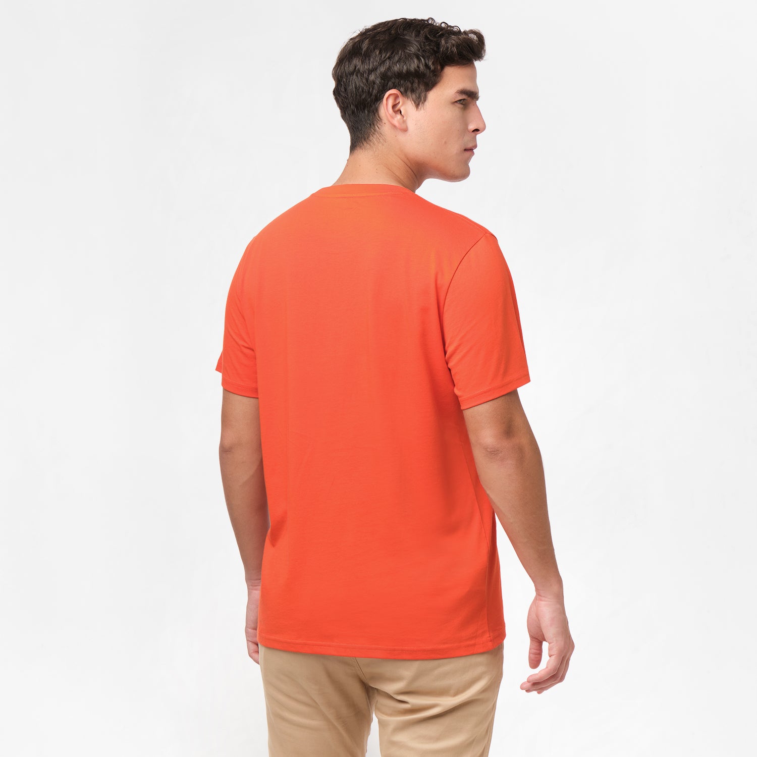 Back view of the man wearing the orange t-shirt, standing with his arms at his sides, paired with beige pants.