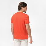 Back view of the man wearing the orange t-shirt, standing with his arms at his sides, paired with white shorts.