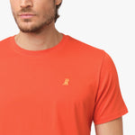 Close-up of the upper chest area of the orange t-shirt, focusing on the small embroidered animal logo near the neckline.