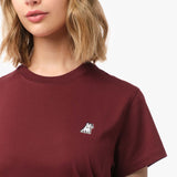 Close-up of the woman's chest area, highlighting the small embroidered logo on the burgundy t-shirt.
