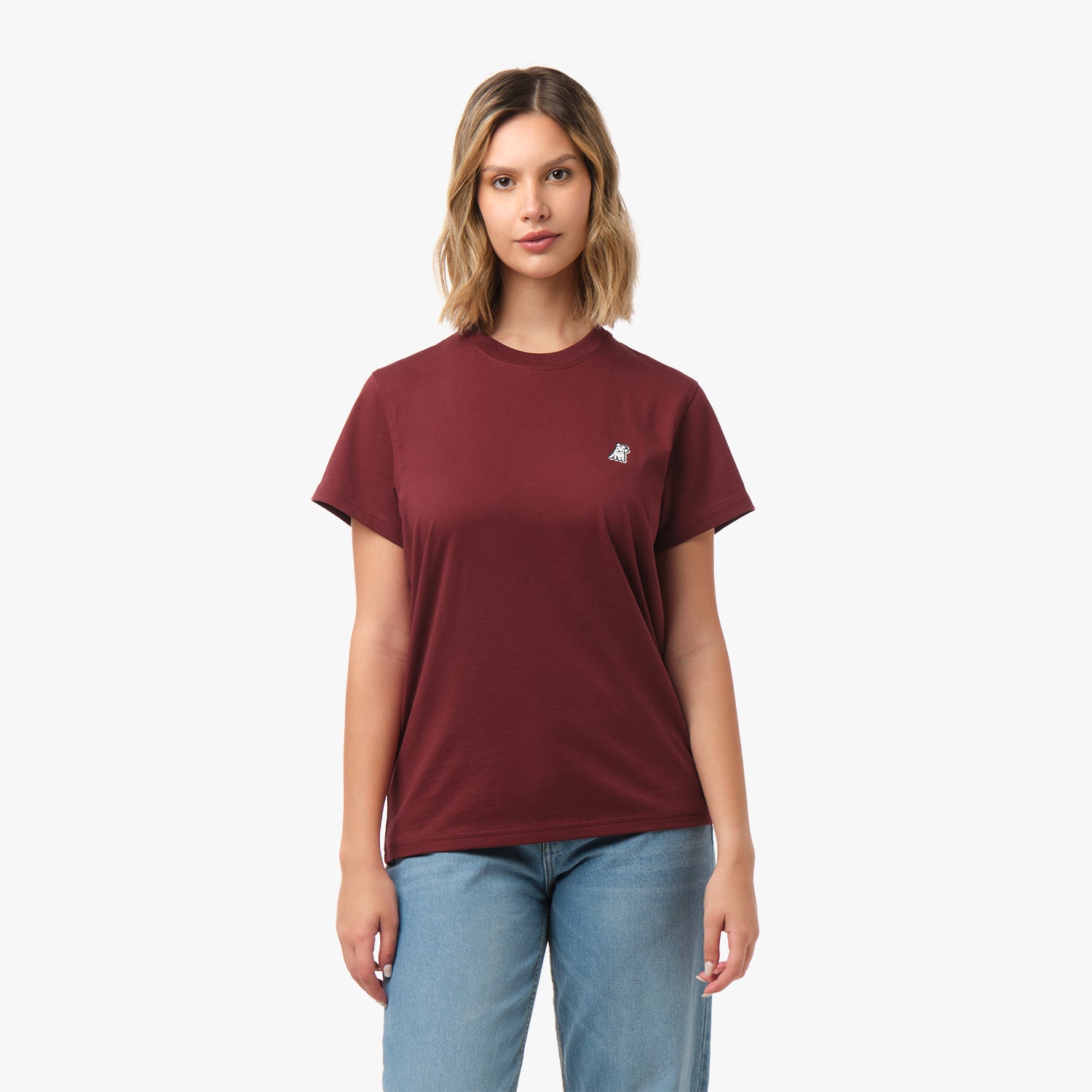 Full front view of a woman wearing the burgundy t-shirt with a small logo on the chest and blue jeans.