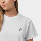 Close-up of the woman's chest area, highlighting the small embroidered logo on the white t-shirt.