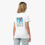 Rear view of a woman wearing a white t-shirt with a large graphic of a beach scene featuring stacked lifeguard chairs and a dog.