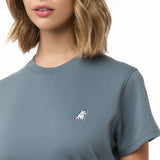 Close-up of the woman's chest area showing the small embroidered logo on the front of the blue-gray t-shirt.
