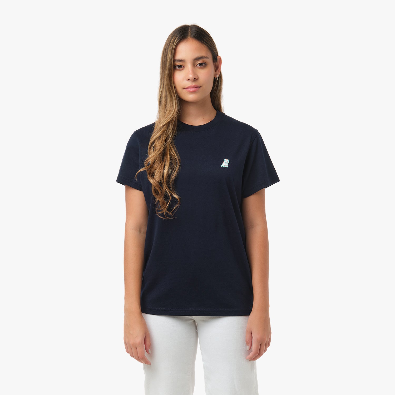 Front view of a woman wearing the navy blue t-shirt with a small embroidered logo on the chest and white pants.