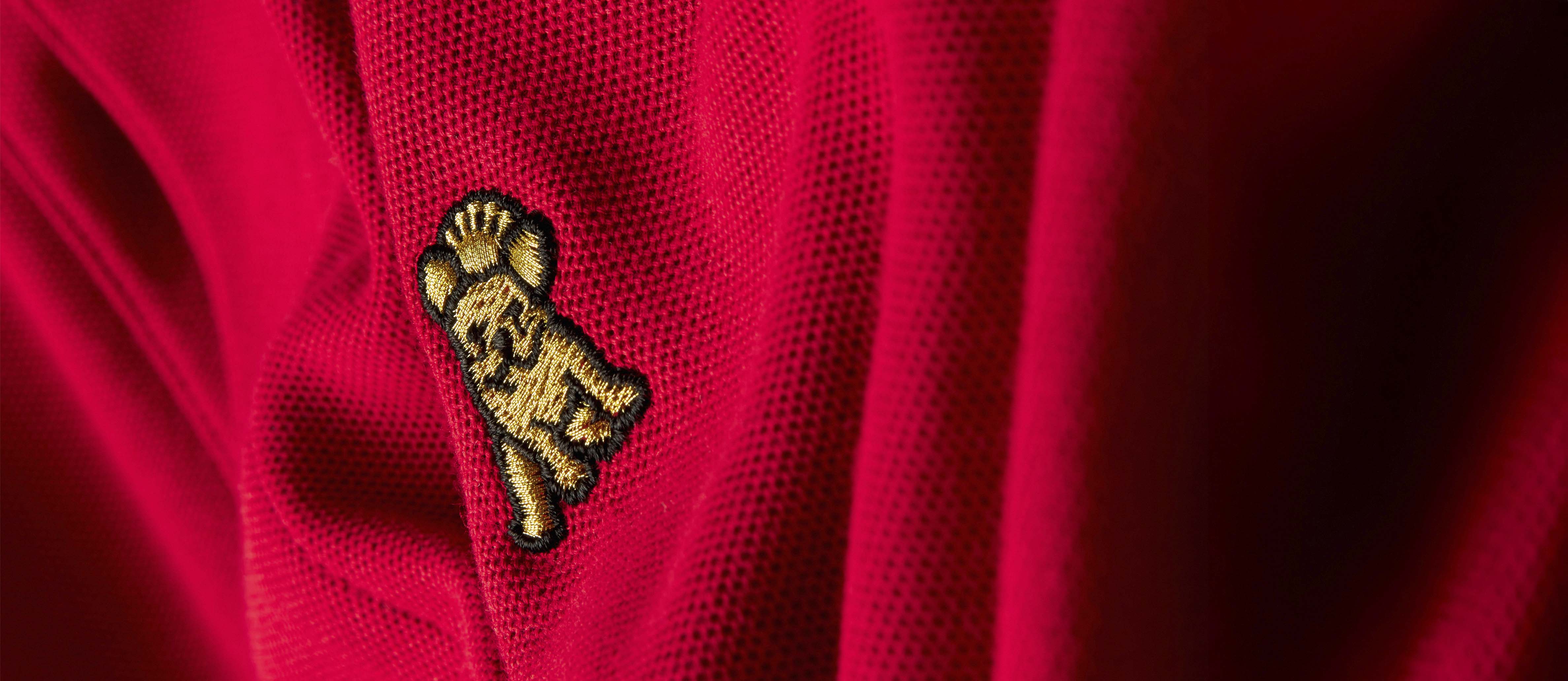 A close-up shows a gold embroidered dog logo with a crown on red pique fabric, likely on a polo shirt