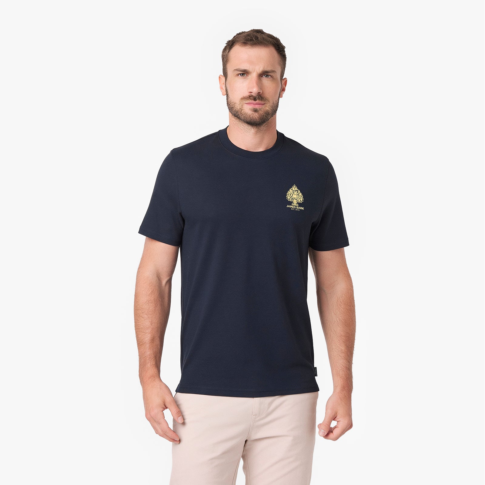 A man wearing a navy blue T-shirt with a small gold spade logo on the left chest