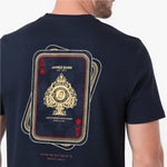 A man wearing a navy blue T-shirt, showing the back of the shirt with a large graphic of stacked playing cards featuring a gold and red design and the text 'JAMES BARK EST. 2025'.