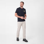 A man modeling a dark navy blue T-shirt with a small yellow logo on the left chest, paired with beige trousers and black sneakers