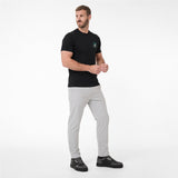 A man modeling a black T-shirt with a small green circular logo on the left chest, paired with light gray trousers and black sneakers