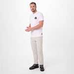 A man modeling a white T-shirt with a small circular graphic on the left chest, paired with beige trousers and black sneakers