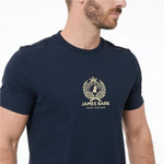 A man wearing a navy blue T-shirt with a gold James Bark logo printed on the chest