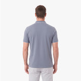 A man viewed from the back wearing a light gray short-sleeve polo shirt with thin white piping on the collar and sleeve cuffs