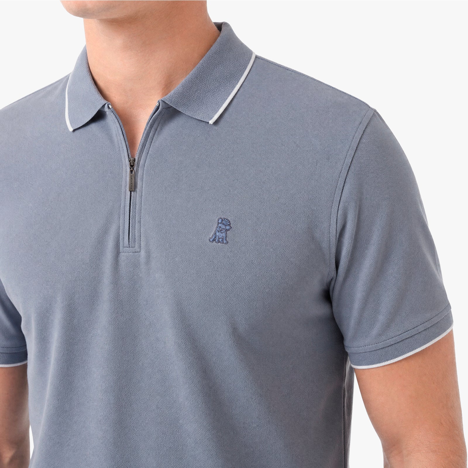 A close-up of a man wearing a slate blue short-sleeve polo shirt with a half-zip collar and white piping trim.
