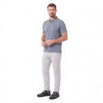 A man modeling a short-sleeve polo shirt in slate blue-gray with light gray trousers and black shoes, standing against a plain white studio background.